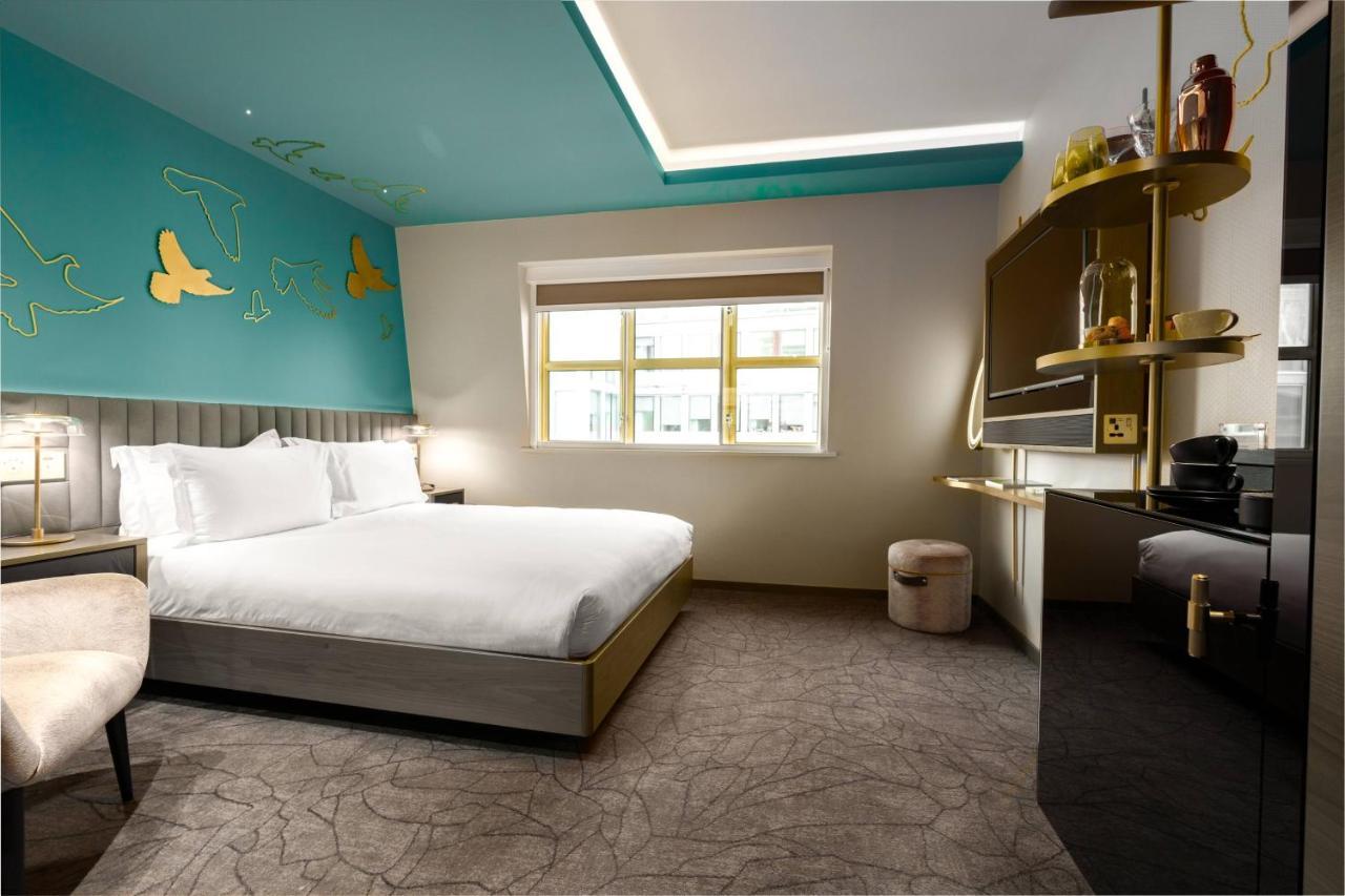 Middle Eight - Covent Garden - Preferred Hotels And Resorts 伦敦 外观 照片 The photo shows a modern hotel room featuring a large bed with white linens positioned against a wall. The decor includes a striking turquoise ceiling and decorative elements, such as yellow motifs, on the wall. There are large windows allowing natur